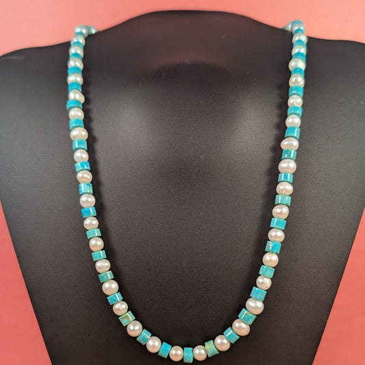 Necklace with turquoise and white beads on a black mannequin against a pink background