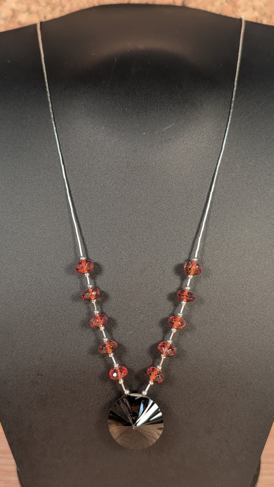 Necklace with red beads and a black and white pendant on a dark stand.