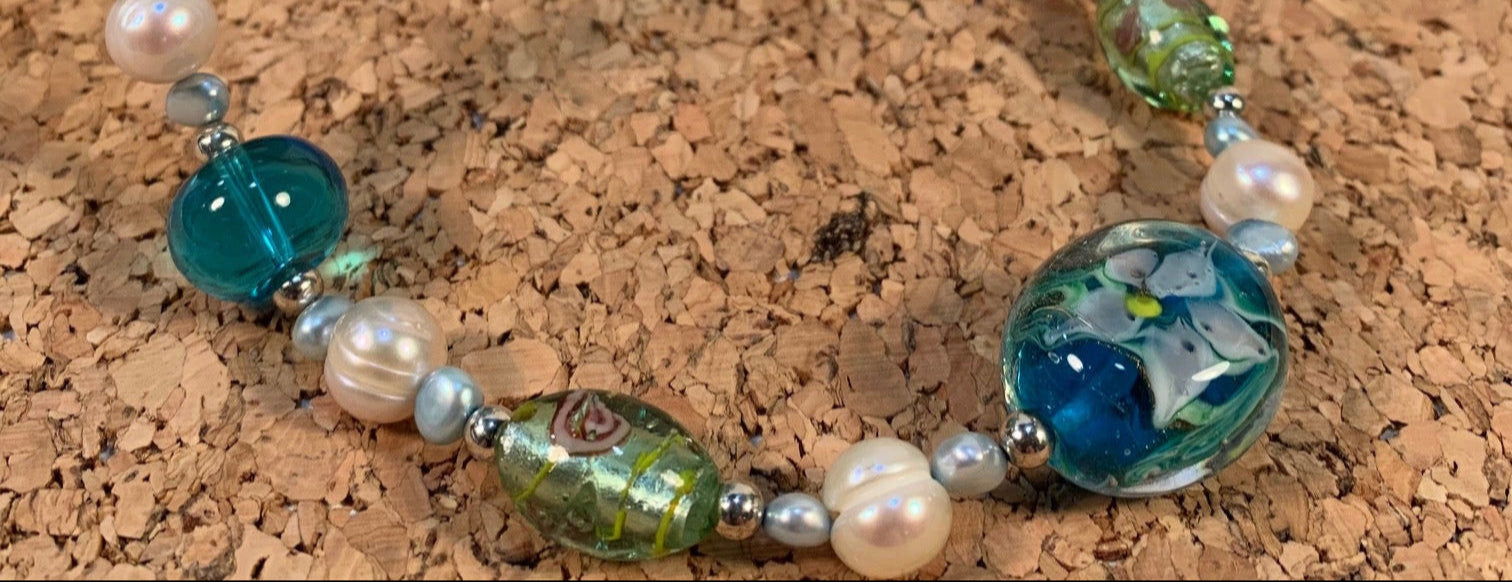 Beaded necklace with green, blue, and pearl beads on a cork surface