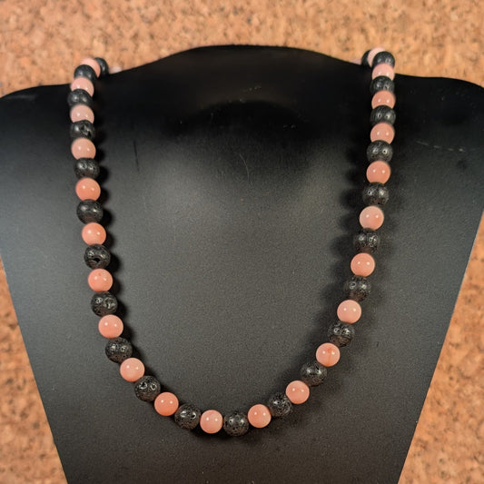Necklace with black and pink beads on a black stand against a wooden background