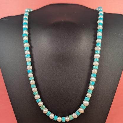 Necklace with turquoise and white beads on a black mannequin against a pink background