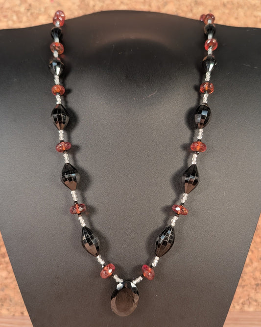 Necklace with black, red, and white beads on a black stand.