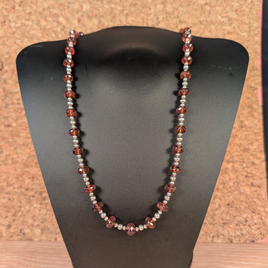 Necklace with red and silver beads on a black stand against a cork background